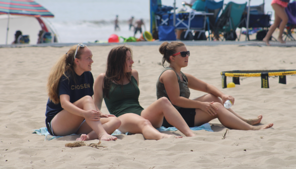 Three students sit on the sand