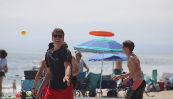 Various activity; a student mid-action in the foreground, Spikeball and a Frisbee hurtling through the air behind him