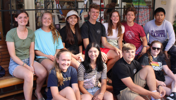 Eleven students pose for a photo on a bench outside a store