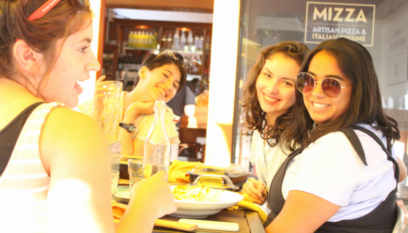 Four pose for a photo at an outdoor table, washed in sunlight