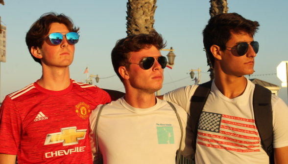 As the sun sets, three straight-faced students in sunglasses pose, gazing into the distance
