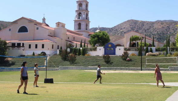 Four toss a football around, with the main campus in the background