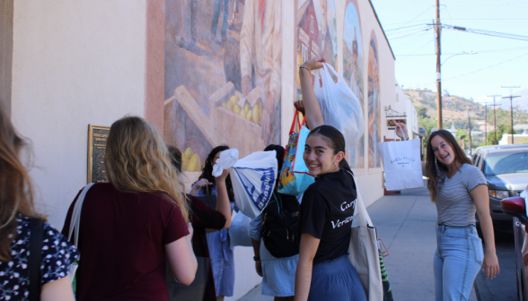 Students pose with their thrift store purchases beside a mural