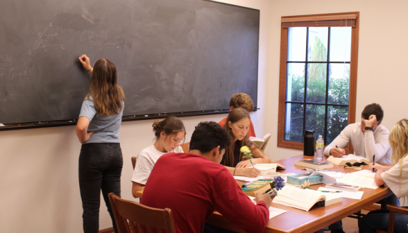 A student practices their prop on the board while others study behind them