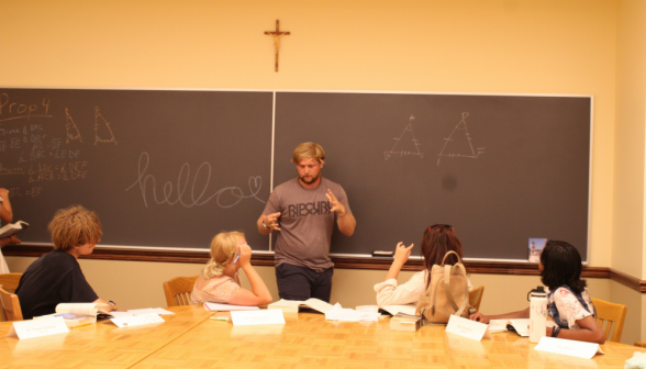 A student gives a practice demonstration of I.4 at a blackboard on which is "Hello" in cursive followed by a heart