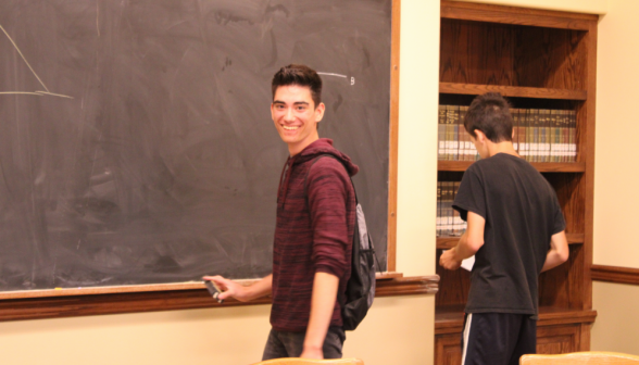 A student turns to smile at the camera as he practices at the board