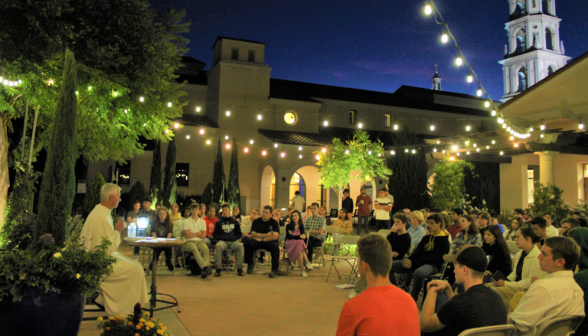 Fr Walshe sits by the Gladys Fountain, lamplit and surrounded by rings of students in chairs