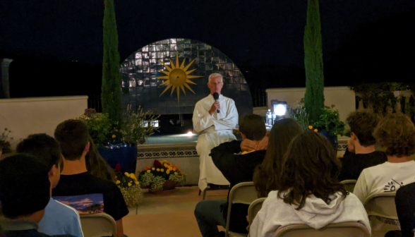 Seated on the side of the fountain, Fr. Walshe addresses the students