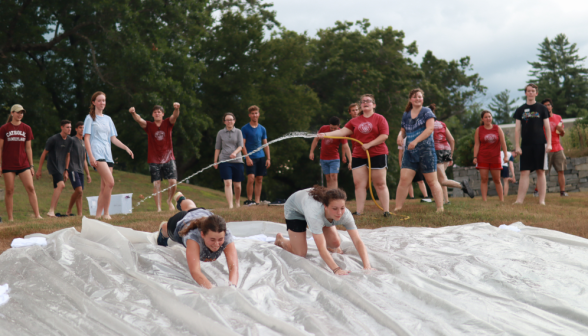 Two dive onto the slide while a prefect sprays water onto it in the background