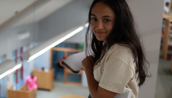 A prefect poses for the camera holding a book over the library's interior balcony