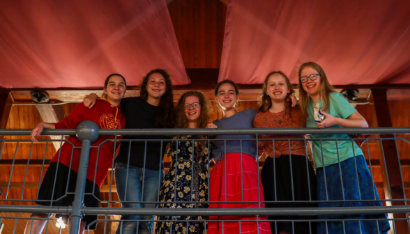 Six pose for a photo at the railing of the upper level