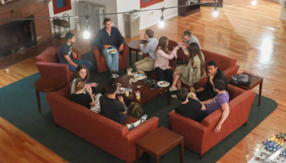 Students chatting on couches and armchairs by the fireplace