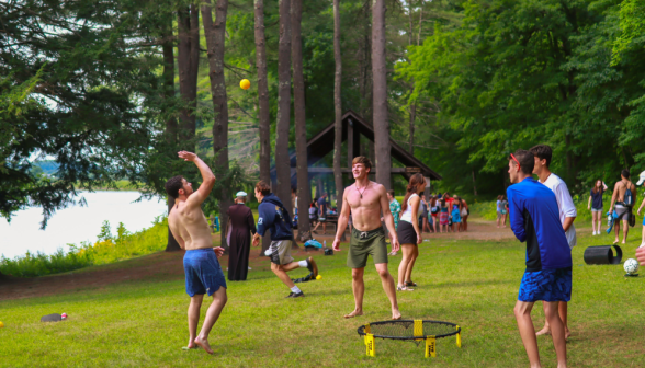 Four men, two shirtless, play Spikeball