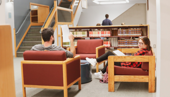 Two studying in armchairs - one smiles for the camera