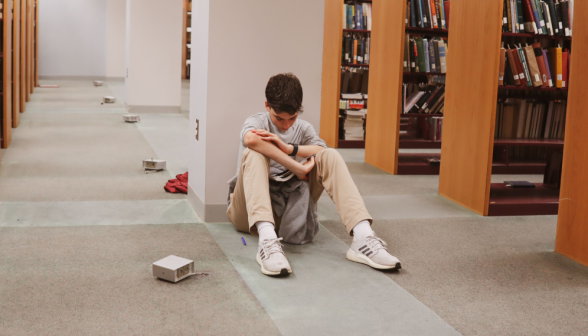 A student studying by a column amid the bookshelves