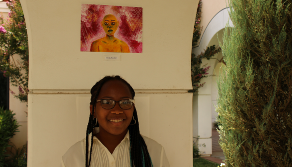 A student poses with her artwork, which depicts a woman surrounded by floral reds