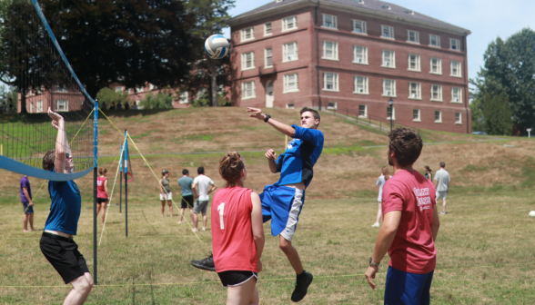 A student hits the ball; Gould visible in the background