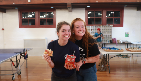 Two pose for a photo with pizza and Cheez-Its