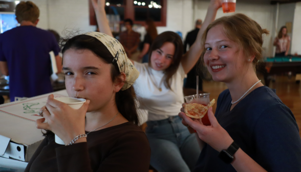 Three pose for the camera with drinks and pizza