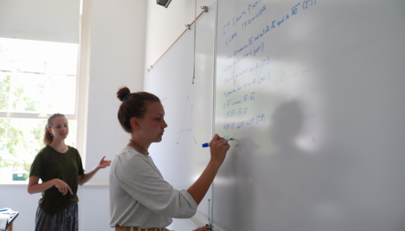 A student practices props at the board, with another in the background
