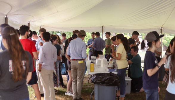 Long shot of clusters of chatting people near the root beer float table