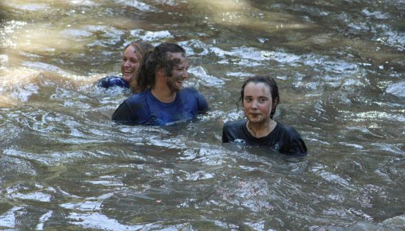 Three students wash off the mud in the pond