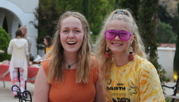 Two pose for a photo, one in striped sunglasses