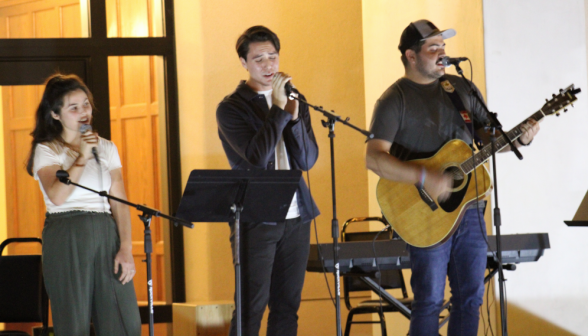 A trio performs, two singing and one on the guitar