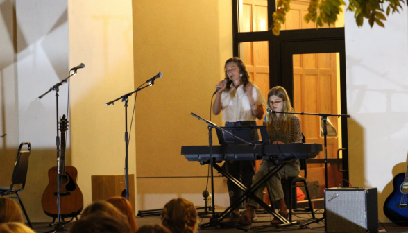 Two perform, one singing and one on the piano