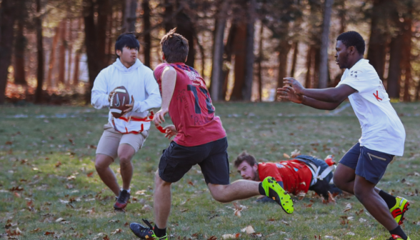 Underclassman catches the ball as upperclassmen rush to intercept and one of his teammates opens for a pass