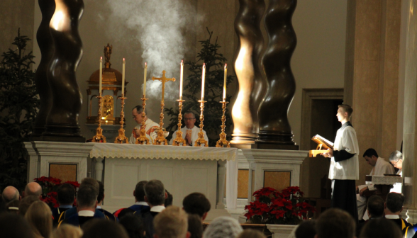 Sunbeams highlight the incense smoke; the priests are at the altar