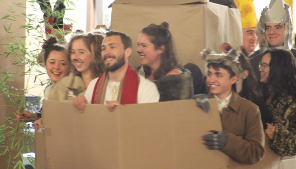 A team of students, mostly dressed as animals, behind a sheet of cardboard
