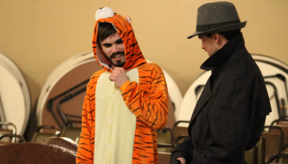 A student in a tiger suit converses with a student in a fedora and black coat