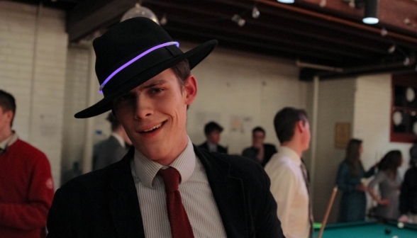 A student poses in a black fedora with a purple glowstick around it like a hatband