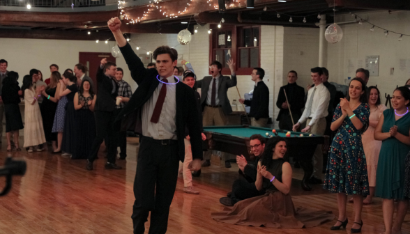 A student cheers wearing a suit, tie, and a purple glowstick necklace