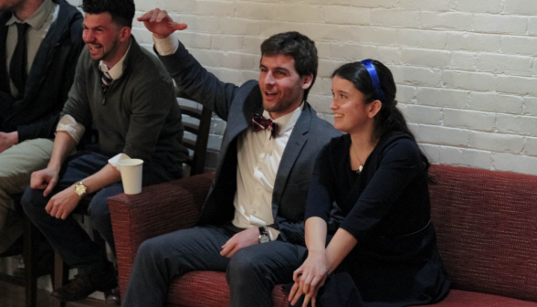 A student couple cheers, seated on the couch