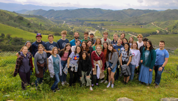 Students pose for a group photo on a green hill outside campus