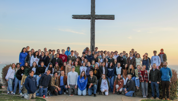 Large group poses afront a wooden cross