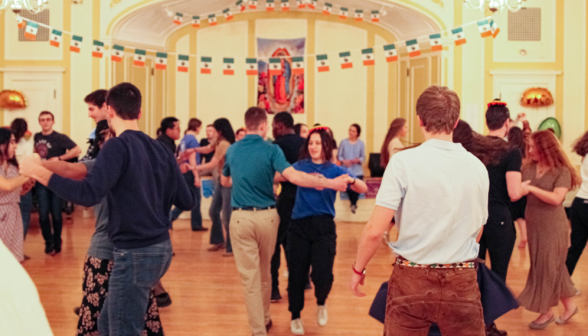 Students dance under strings of Mexican flags and a poster of Our Lady of Guadalupe