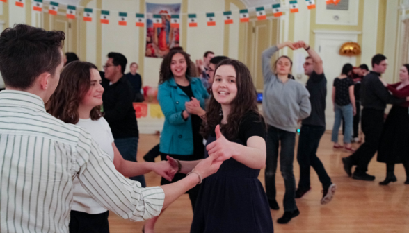 Students dance under strings of Mexican flags and a poster of Our Lady of Guadalupe