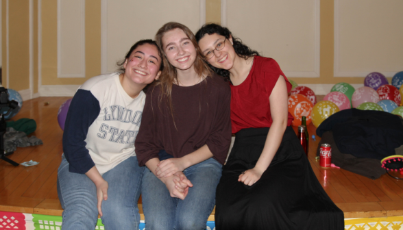 Three pose for a photo, seated on the stage