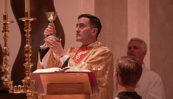 The priest holds up the chalice