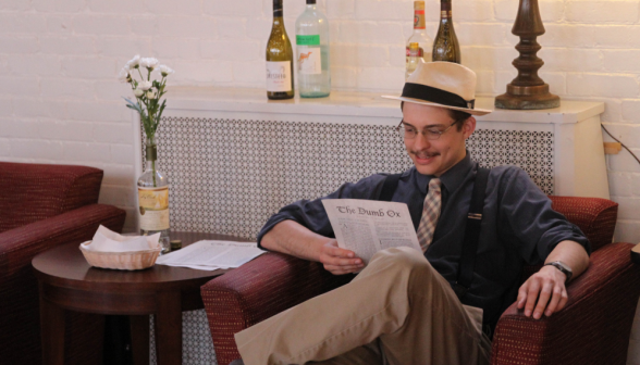 A guest chuckles, reading the newspaper in an armchair