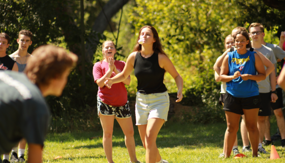 A student carries an egg in a spoon in her mouth while her section mates cheer her on