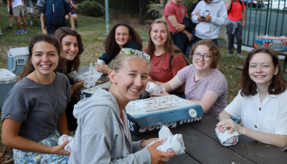 Seven smile for the camera around a box of Jersey Mike's sub sandwiches