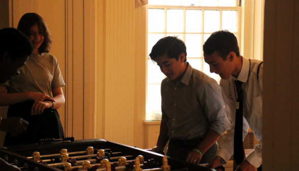 Three play foosball while one looks on