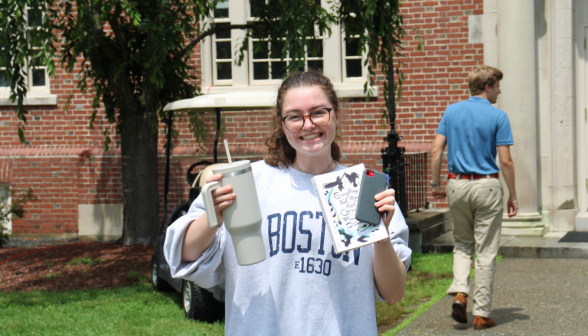 A student poses with book, phone, and a large vacuum flask with a straw