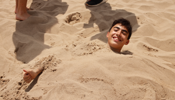 A student buried to the neck in sand gives a thumbs-up