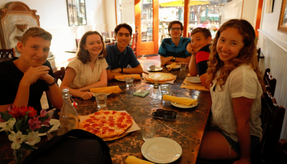 Six at a restaurant table around a pizza