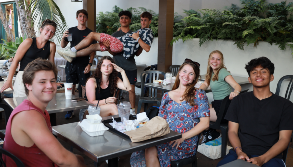 Nine pose together at an outdoor table